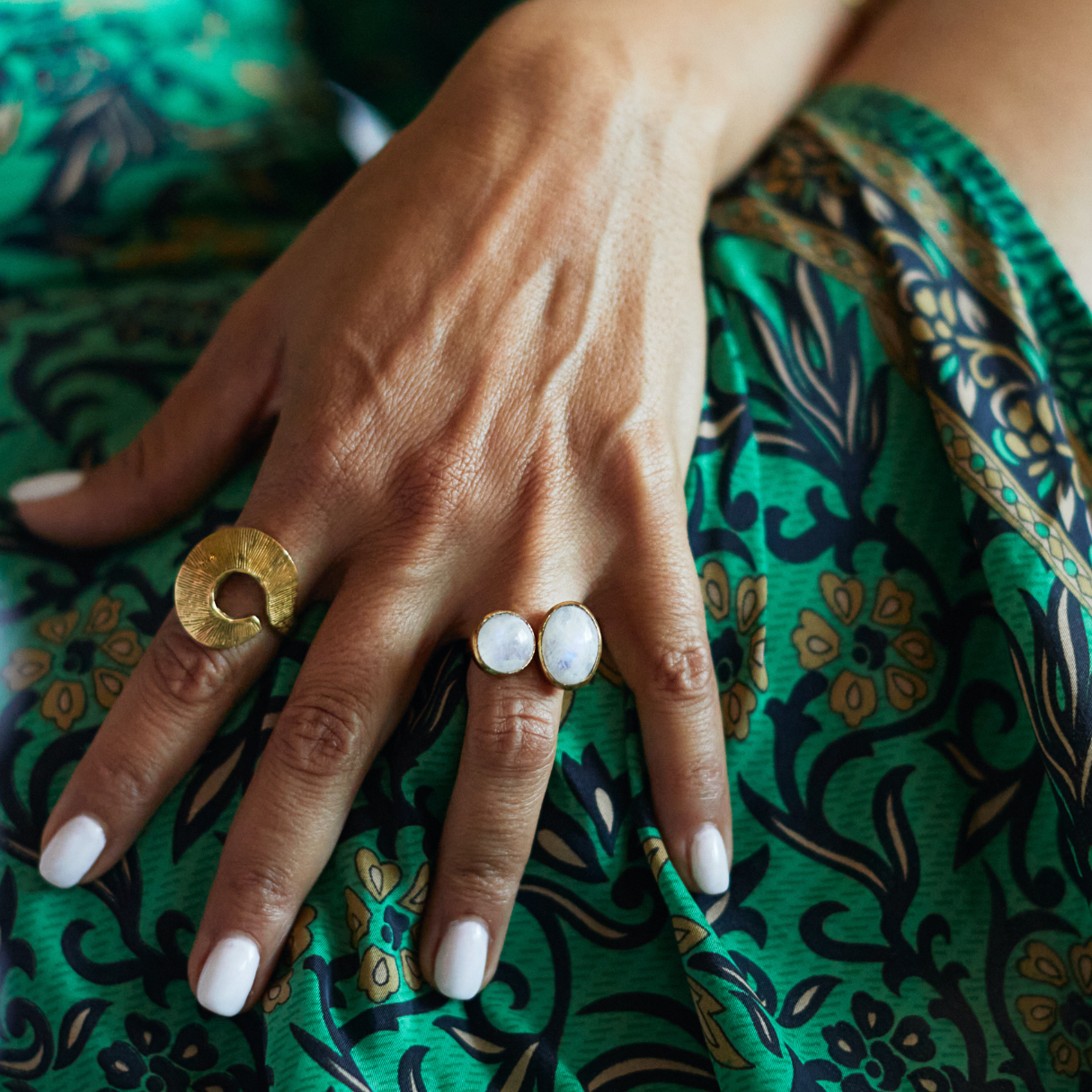 Hand with gold and white rings on a green patterned fabric background