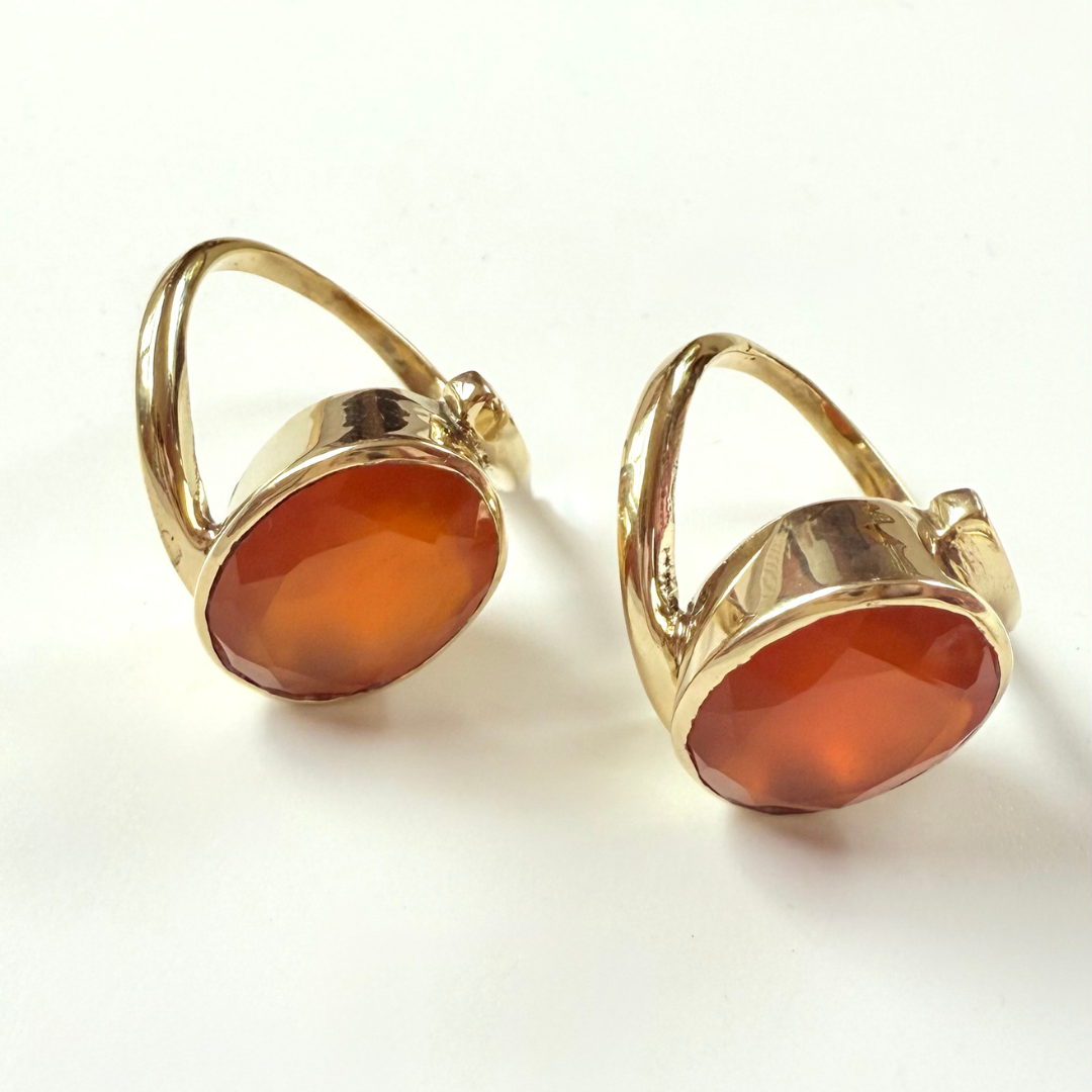 Gold earrings with orange carnelian gemstones on a white background