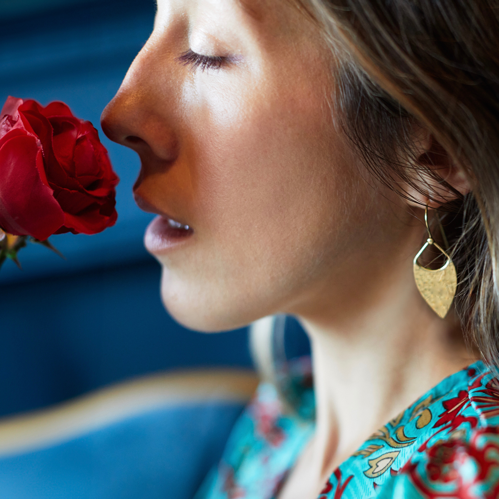 Woman smelling a red rose with a blurred blue background