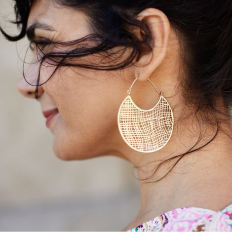 Close-up of a woman wearing gold circle web earrings with a blurred background