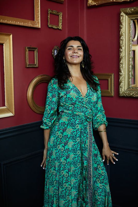 Woman in a green dress standing against a red wall with gold frames