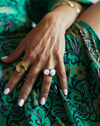 Hand with gold and white rings on a green patterned fabric background