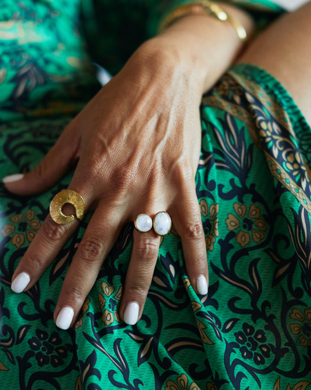 Hand with gold and white rings on a green patterned fabric background