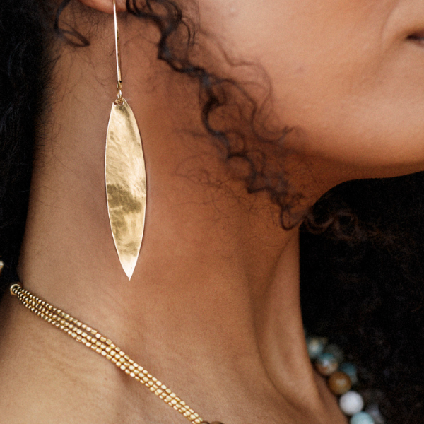 A close-up of a woman''s neck and side profile wearing a hammered gold drop earring and a matching gold beaded necklace.