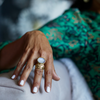 Hand wearing a gold ring with a large moonstone, against a blurred background.